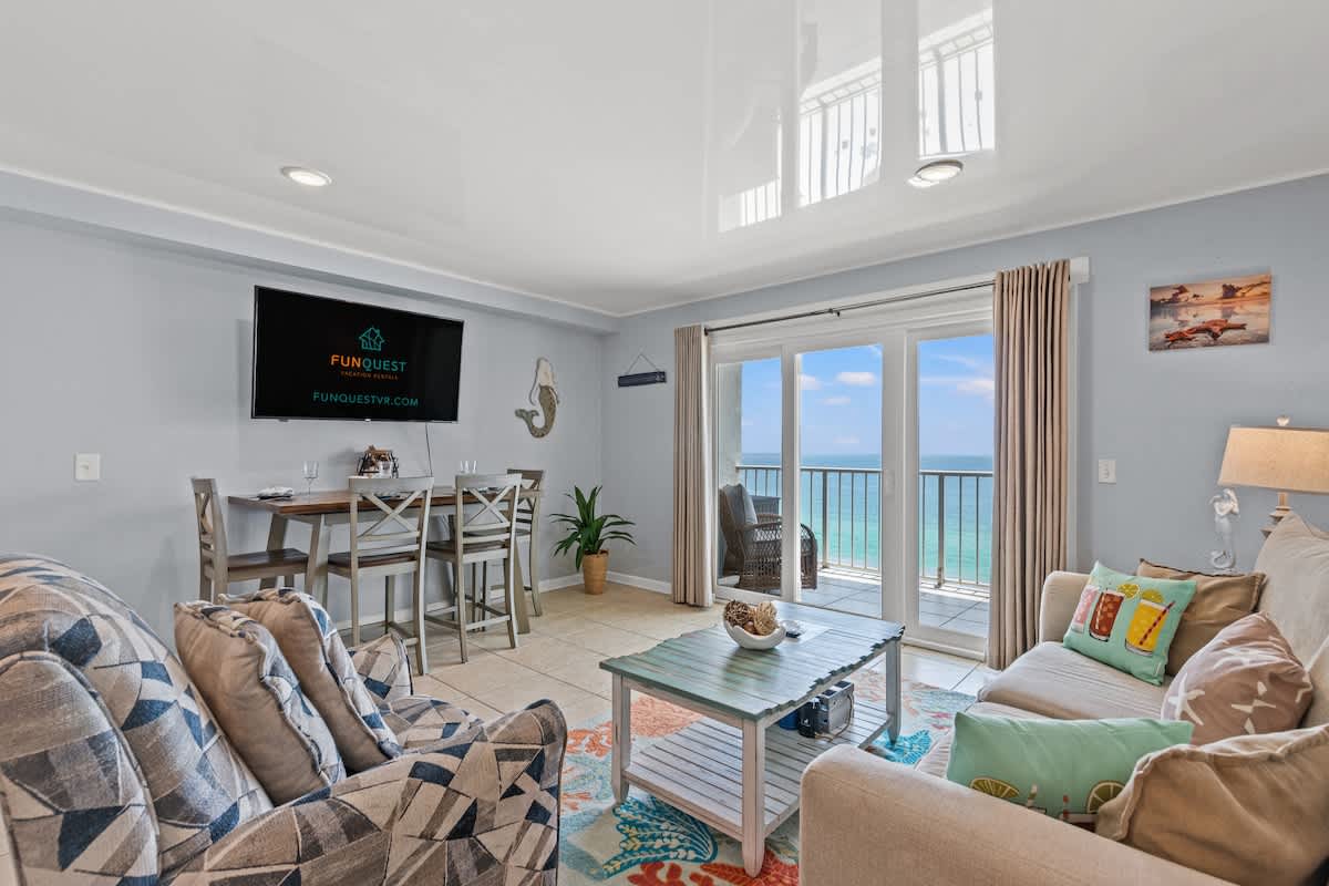 The Summit 1409 – Modern living room with ocean view, TV, dining table, and balcony access.
