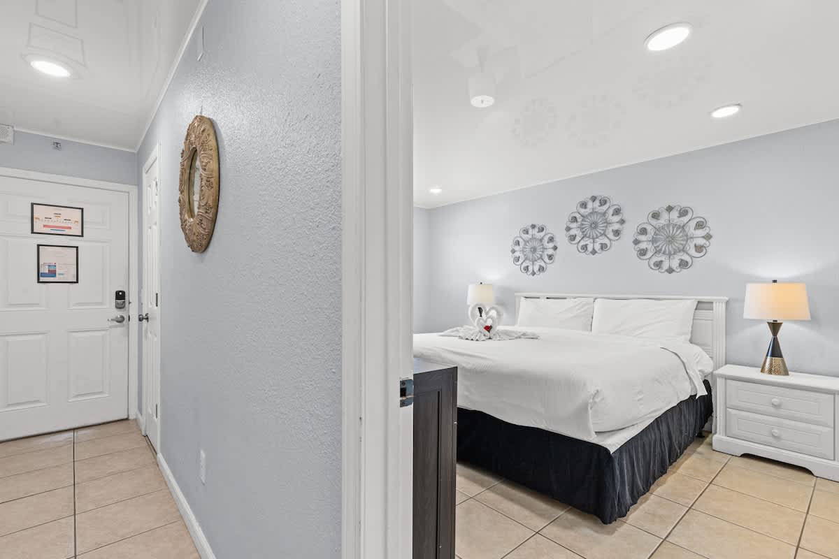 The Summit 1409 – Bedroom with a king bed, bedside lamps, and decorative wall art, visible from a hallway.