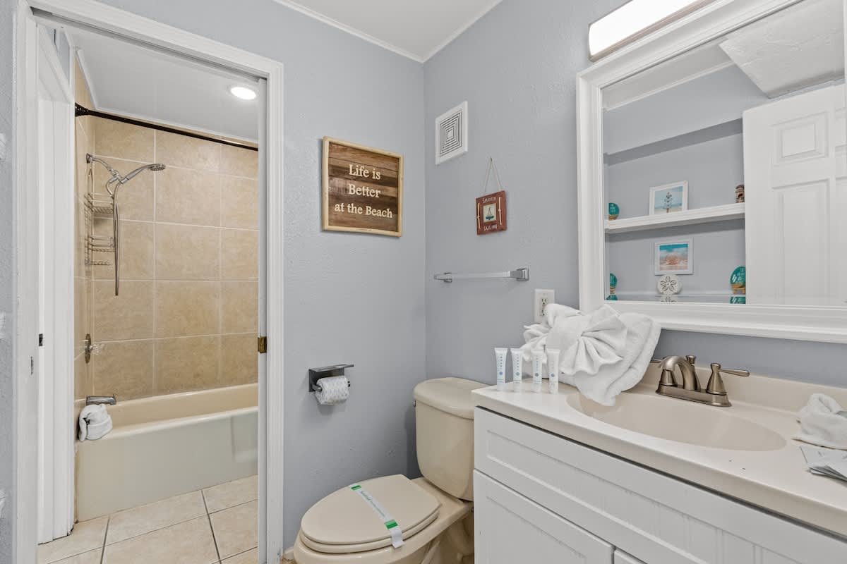 The Summit 1409 – Bathroom featuring a bathtub, toilet, sink, and decorative beach-themed wall art.