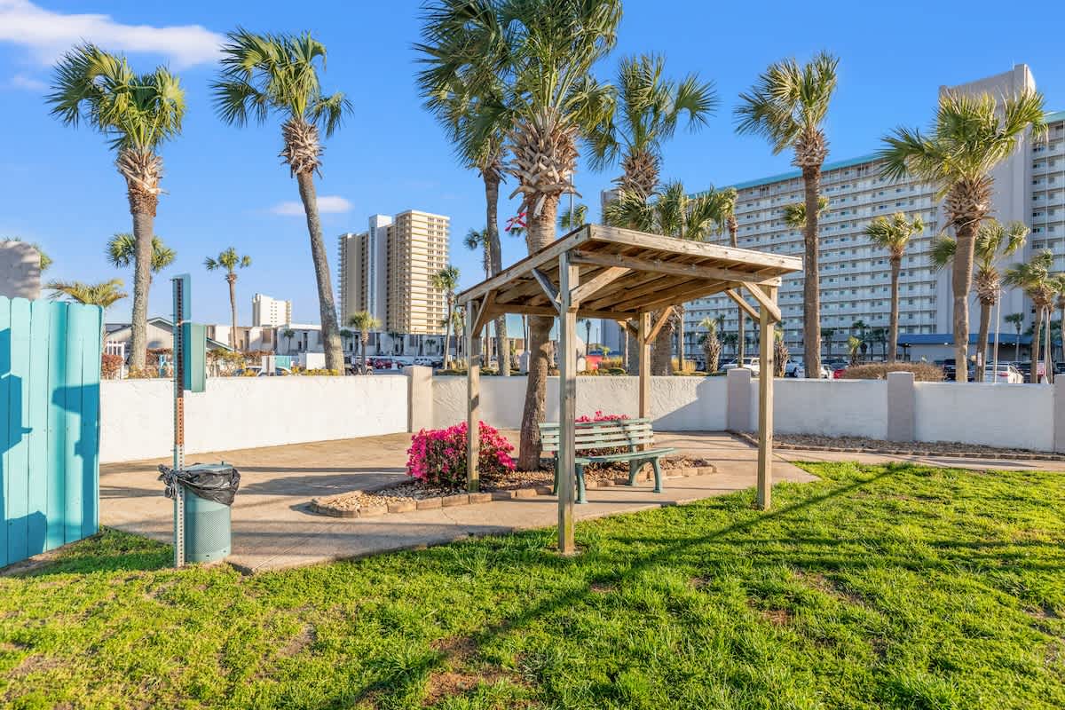 The Summit 1409 – Outdoor seating area with gazebo, palm trees, flowers, and nearby high-rise buildings under a clear blue sky.