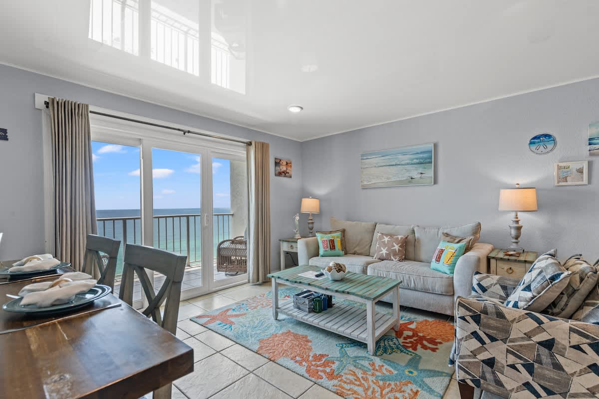 The Summit 1409 – Living room with ocean view, sofa, armchairs, coffee table, and dining table set for four.