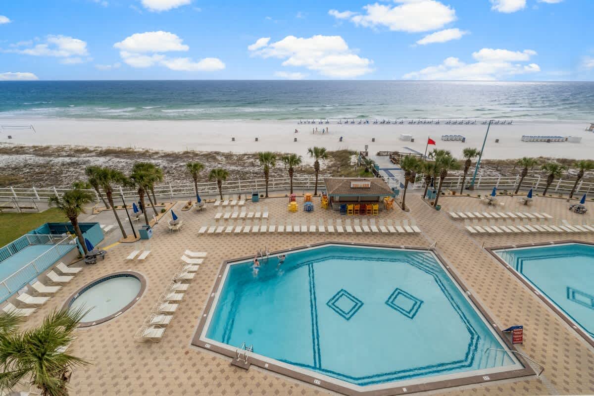 The Summit 620 – View of outdoor pools and beach with palm trees and lounge chairs.