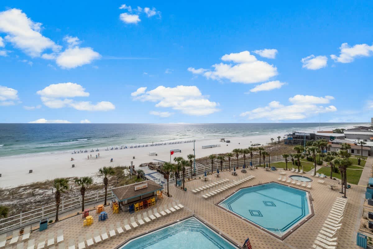 The Summit 620 – Beachfront view with two swimming pools, lounge chairs, and palm trees under a clear blue sky.