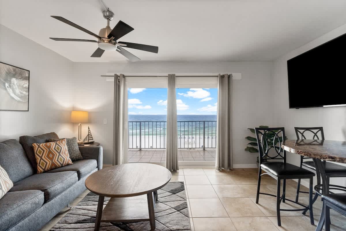 The Summit 620 – Living room with gray couch, dining table, and balcony view of the beach and ocean.