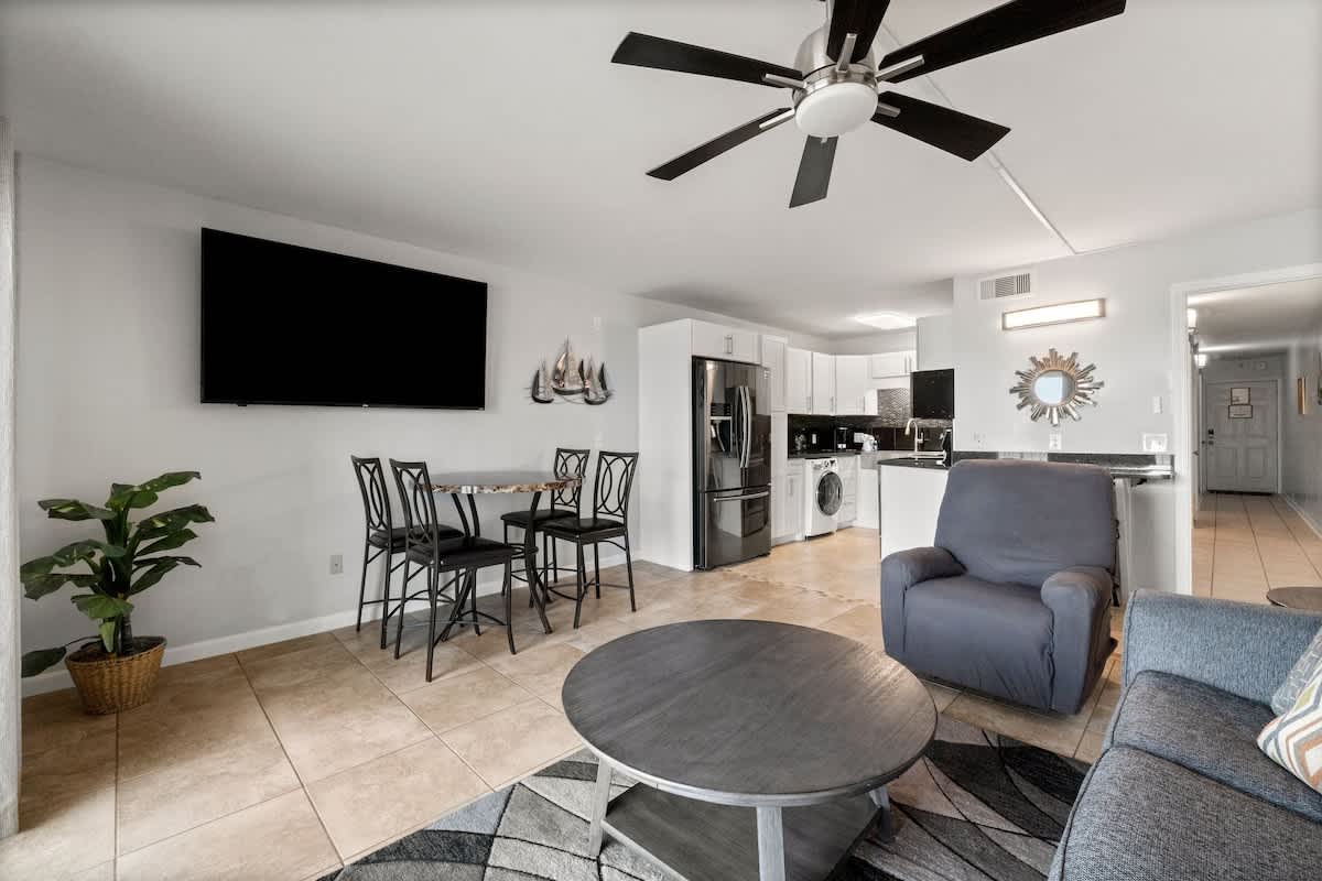 The Summit 620 – Living room with a couch, coffee table, dining table, kitchenette, and wall-mounted TV.