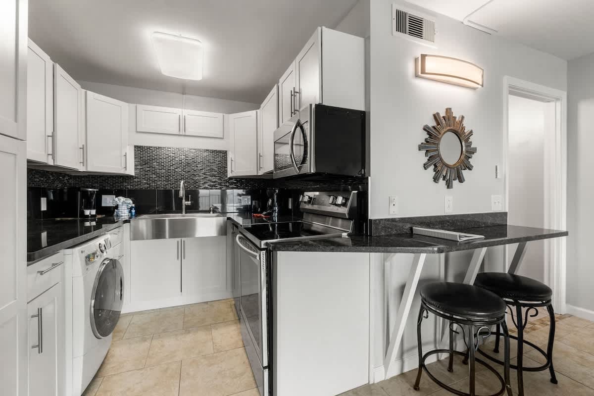 The Summit 620 – Modern kitchen with black countertops, stainless steel appliances, bar seating, and tiled backsplash.