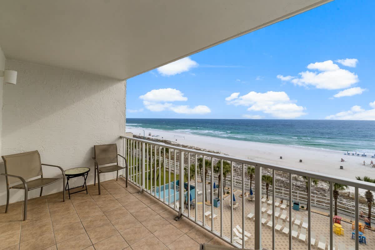 The Summit 620 – Balcony view with two chairs overlooking the beach and ocean, with a pool area below.