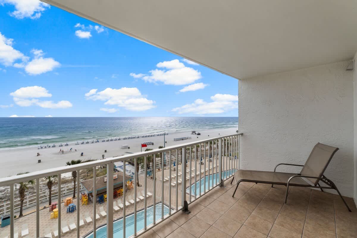 The Summit 620 – Balcony view overlooking the beach, pools, and ocean under a blue sky with clouds.