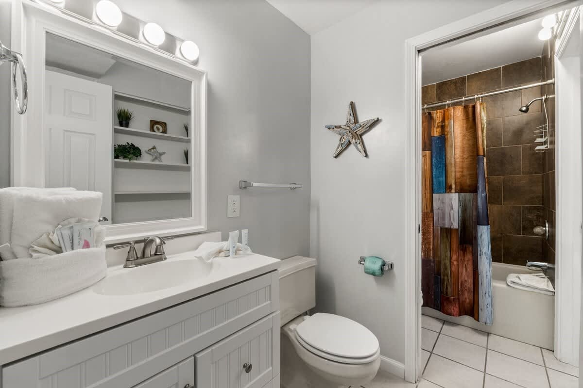 The Summit 620 – Bathroom with white vanity, large mirror, shower with patterned curtain, and shelves with decor.