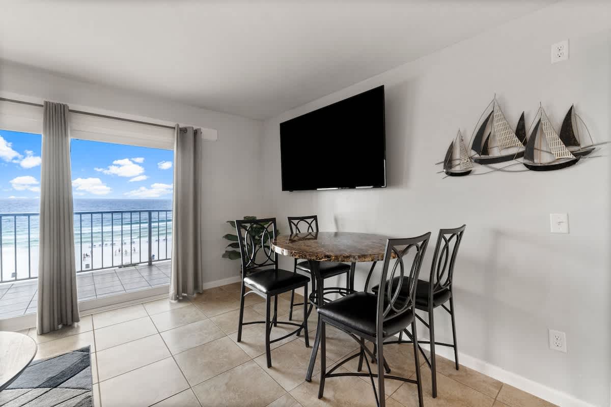 The Summit 620 – Dining area with round table, black chairs, large TV, and ocean view through sliding glass door.