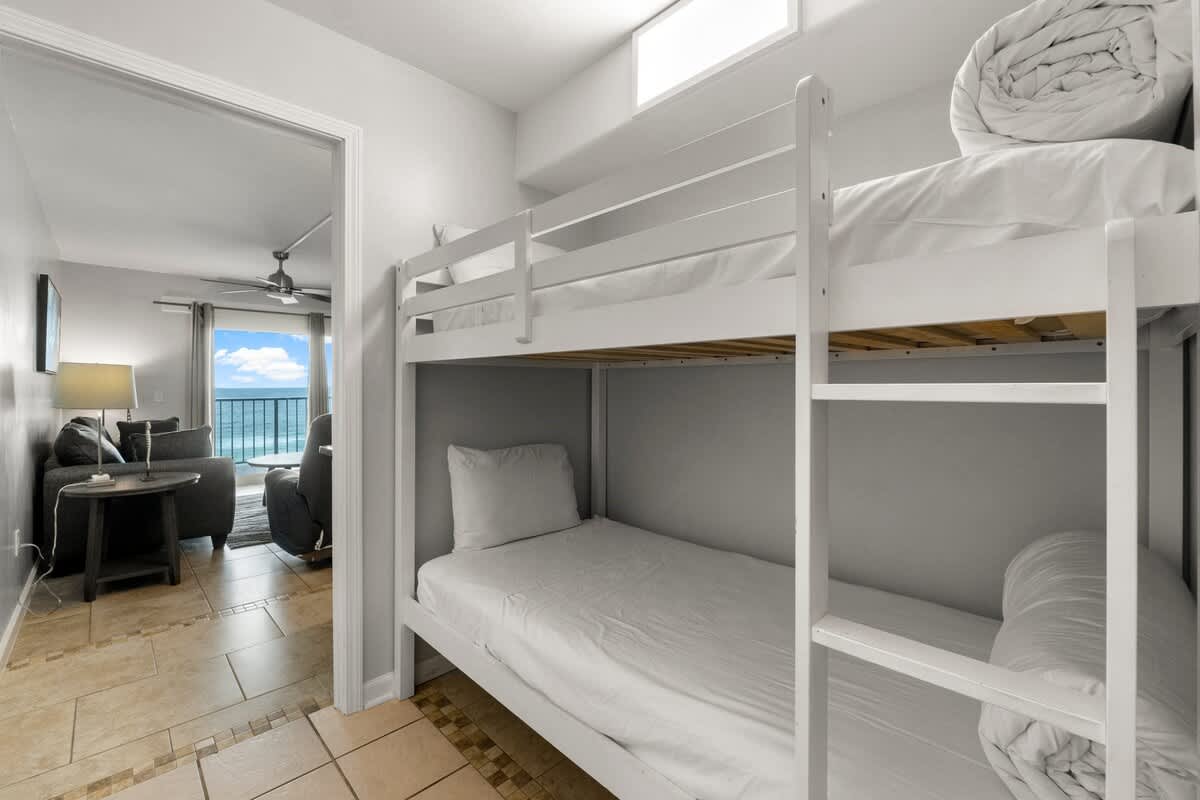The Summit 620 – Bunk beds in a room with a view of the ocean, adjacent living area with grey couch.