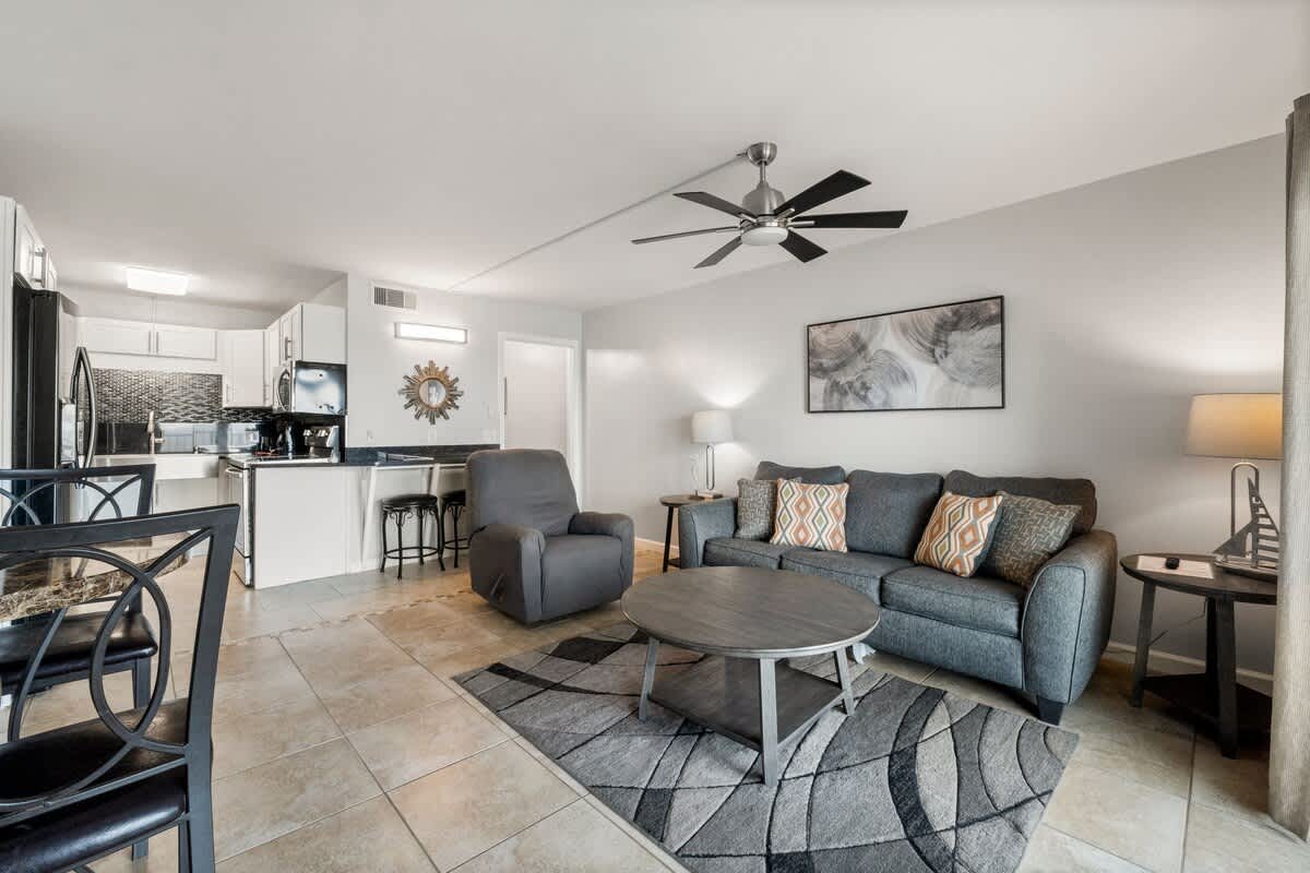 The Summit 620 – Living room with gray sofa, coffee table, dining area, kitchen, and ceiling fan.