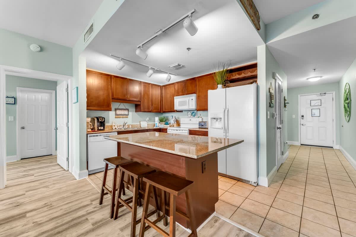 Laketown Wharf 1331 – Open kitchen with wooden cabinets, granite island, and seating, leading to tiled entrance area.