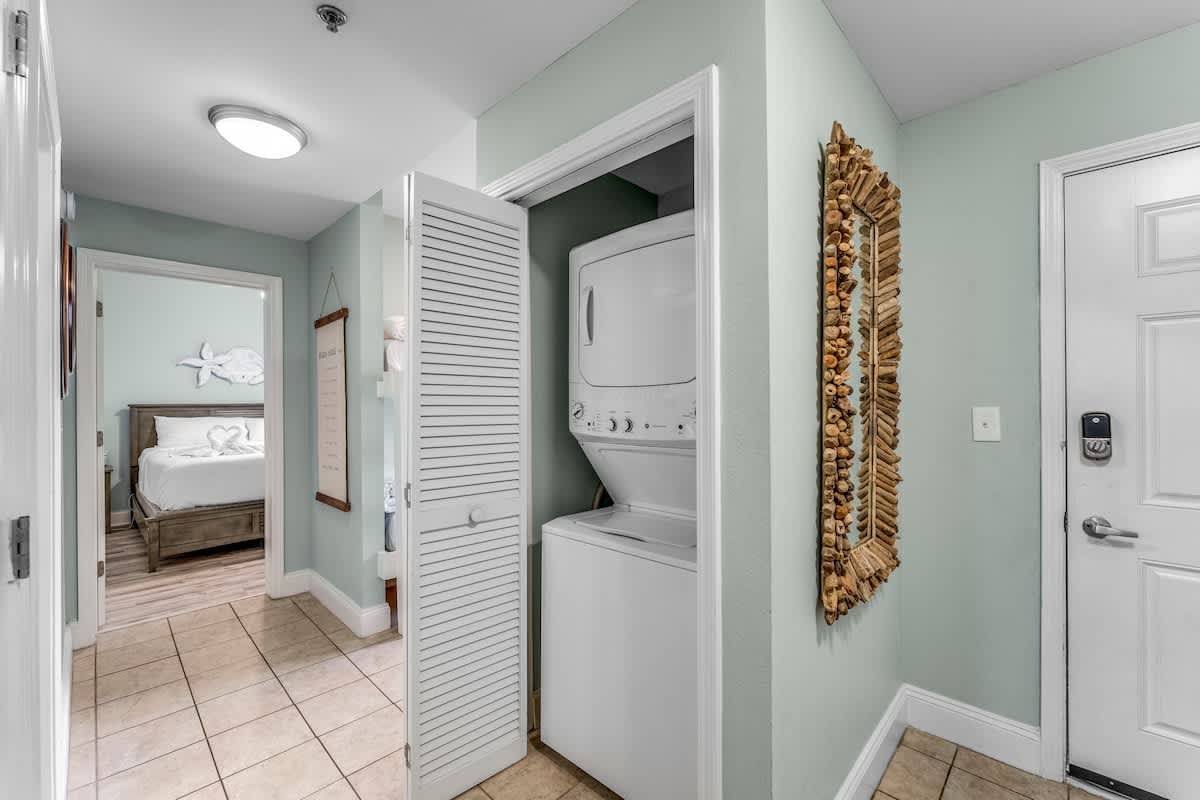 Laketown Wharf 1331 – Hallway with laundry area, framed mirror, and view into bedroom with a bed visible.