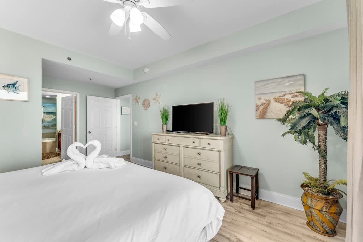 Laketown Wharf 1331 – Cozy bedroom with king bed, TV, decorative accents, and a view of the en-suite bathroom.