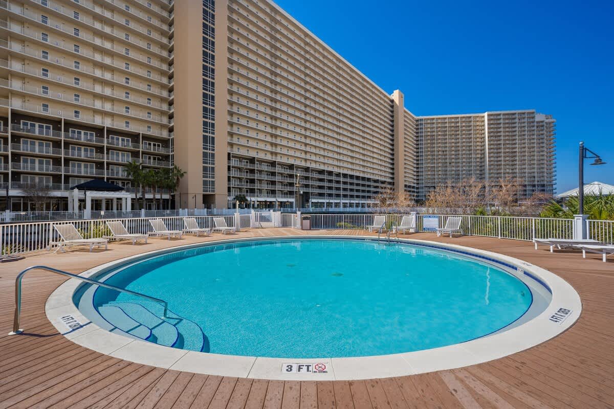 Laketown Wharf 1331 – Circular swimming pool in front of a large multi-story building with lounge chairs and a clear blue sky.
