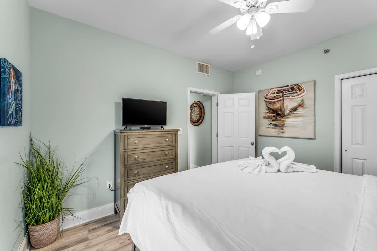 Laketown Wharf 1331 – Bedroom with a king bed, dresser, TV, and artwork on mint green walls.