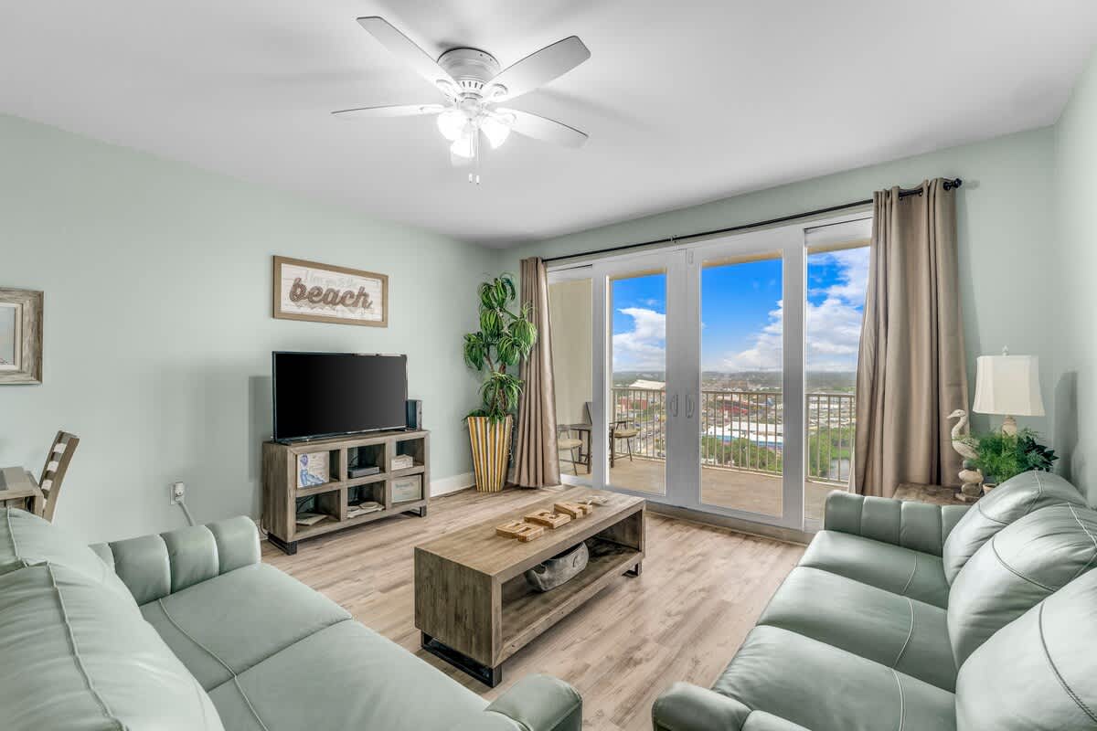 Laketown Wharf 1331 – Living room with light green walls, two couches, TV, coffee table, and sliding doors opening to a balcony view.