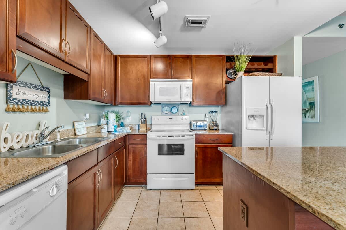 Laketown Wharf 1331 – Modern kitchen with wooden cabinets, granite countertops, appliances, and beach-themed decor.