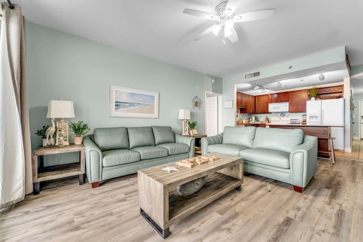 Laketown Wharf 1331 – Living room with light blue couches, wooden coffee table, and kitchen visible in the background.