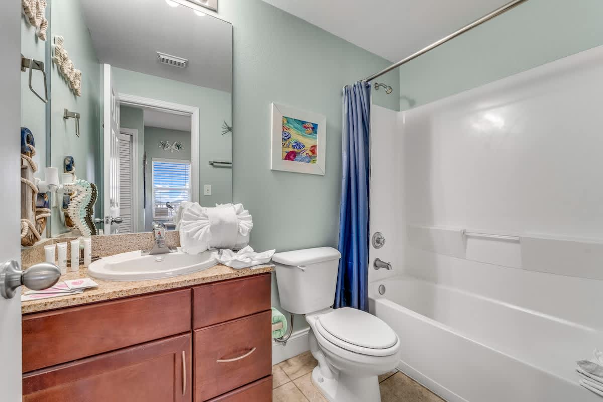 Laketown Wharf 1331 – Bathroom with beige tile floor, wooden vanity, mirror, shower curtain, and decorative items.