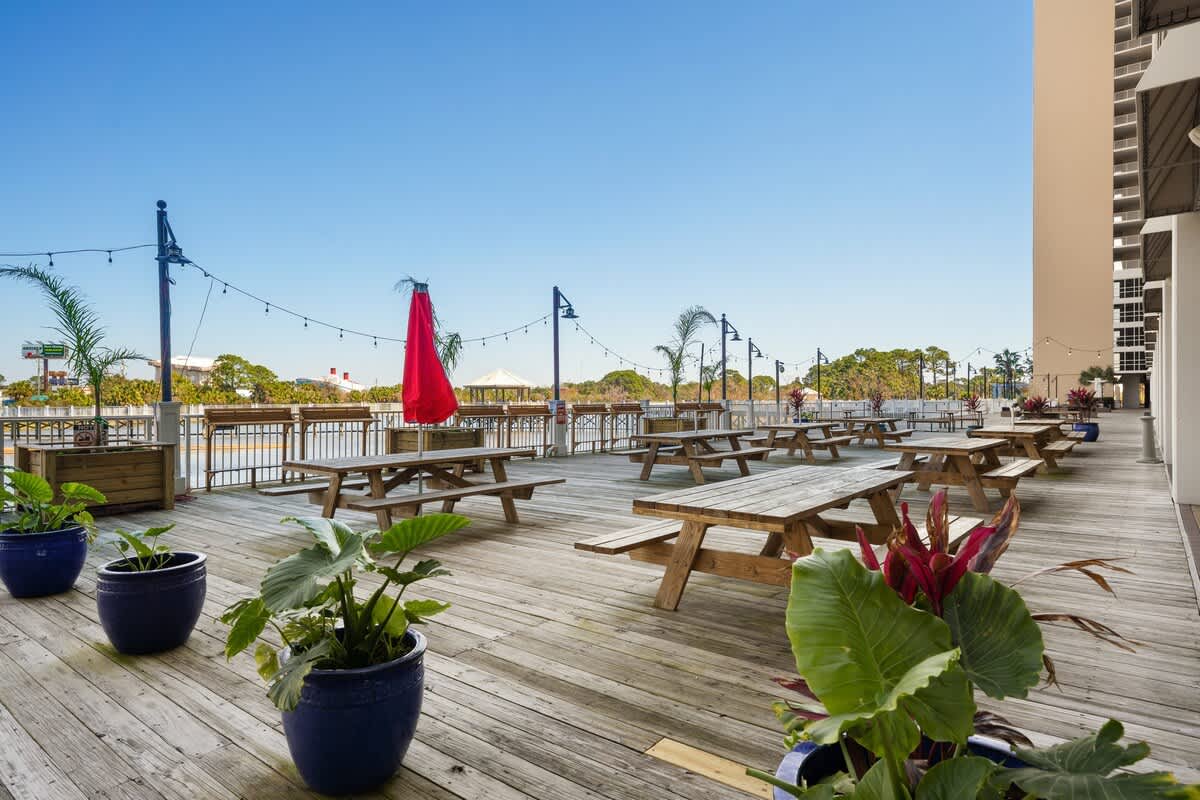 Laketown Wharf 1331 – Outdoor terrace with wooden tables, potted plants, and view of water under a clear blue sky.