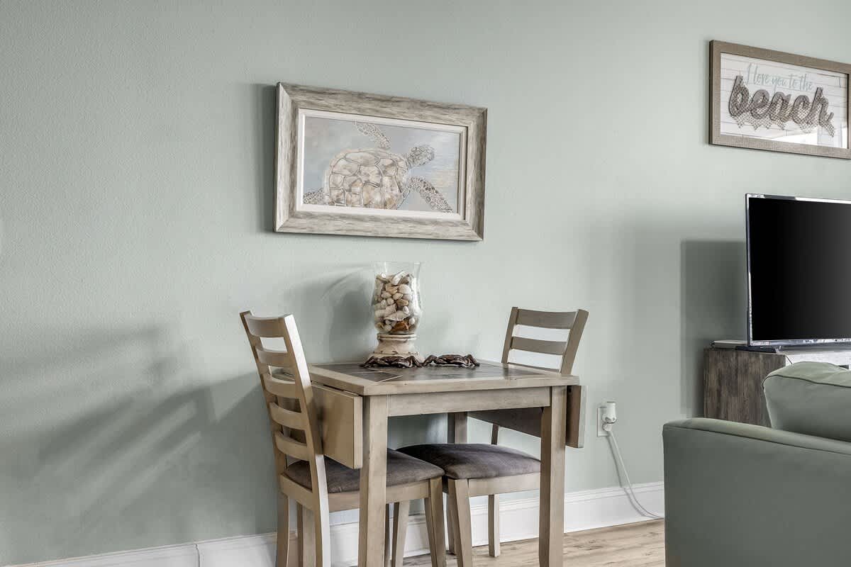 Laketown Wharf 1331 – Dining table with two chairs, decorated wall art, and a television in a light-colored room.
