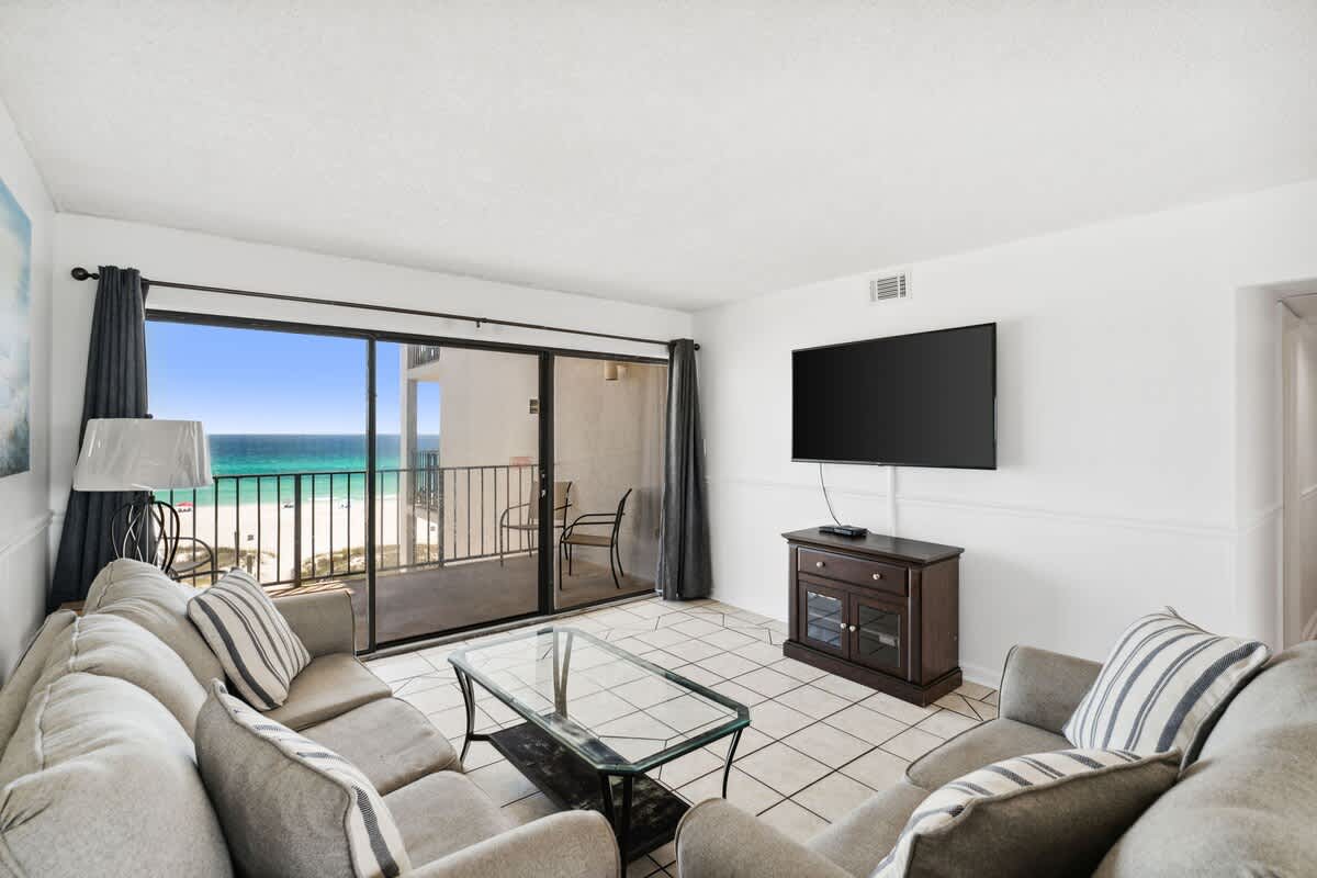 Moondrifter 608 – Living room with a couch, glass table, TV, and sliding doors showcasing ocean view.