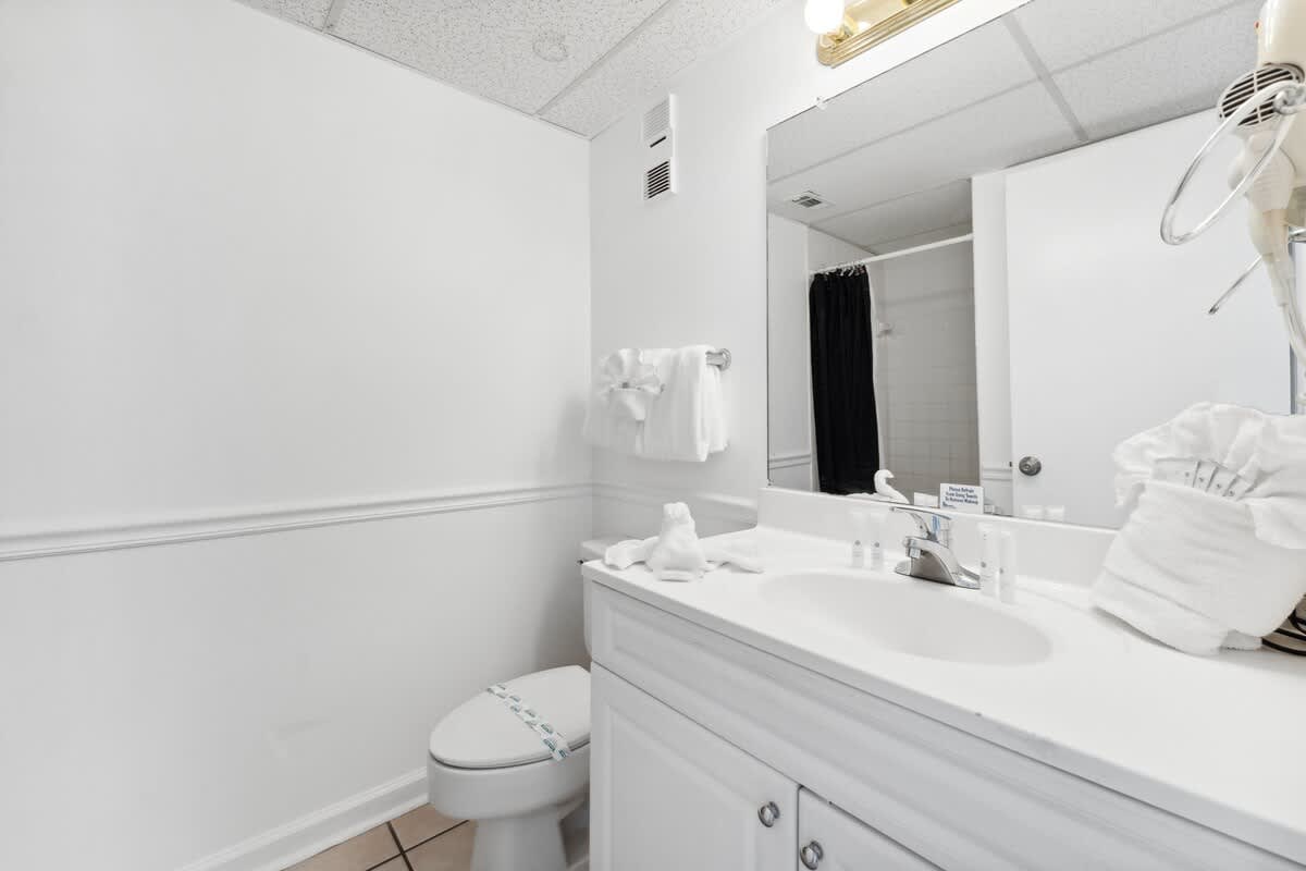 Moondrifter 608 – Clean bathroom with a sink, toilet, white towels, and a black shower curtain.