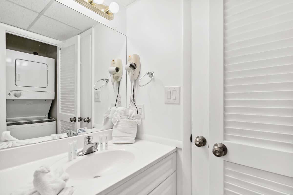 Moondrifter 608 – Bathroom with sink, towels, hairdryer, laundry units behind closed doors, and wall lighting.