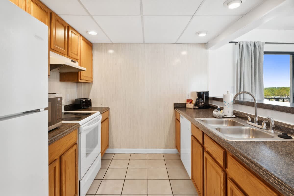 Moondrifter 608 – Kitchen with wooden cabinets, granite countertops, sink, and appliances, featuring a window view.