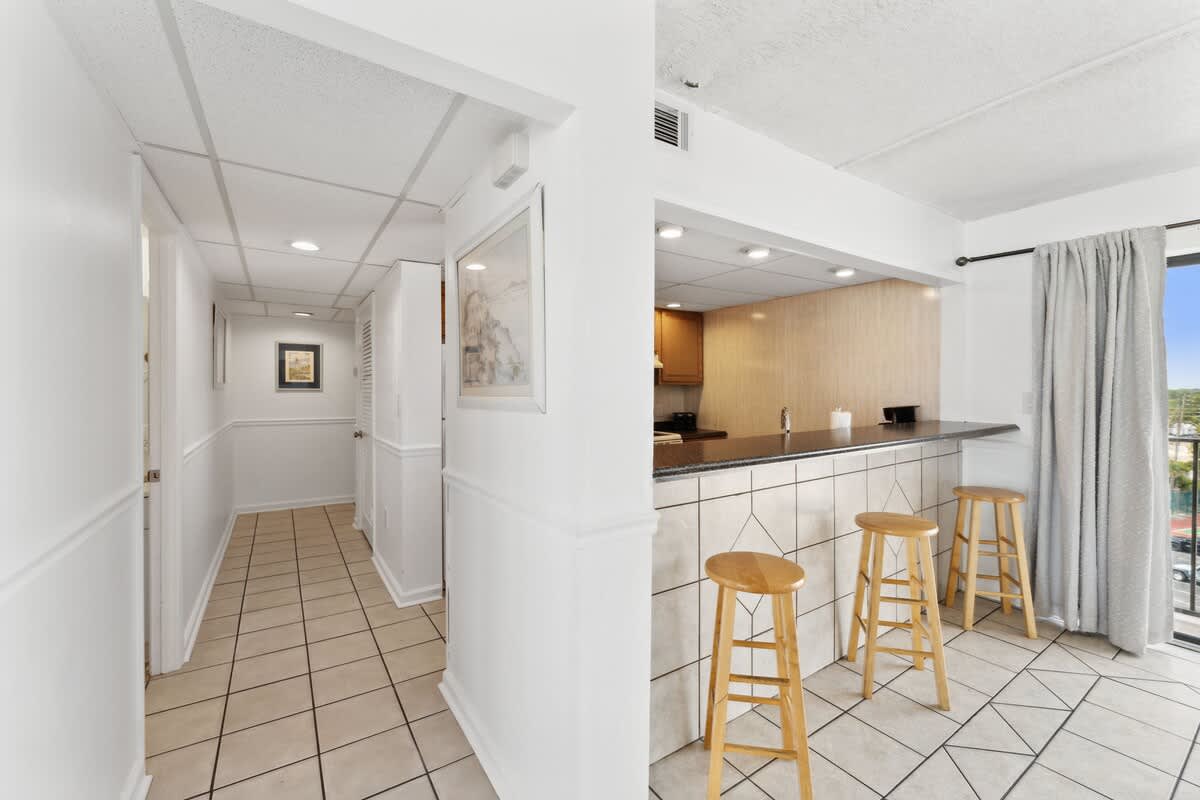 Moondrifter 608 – Interior view of a vacation rental with a kitchen bar, tiled floor, and hallway leading to additional rooms.