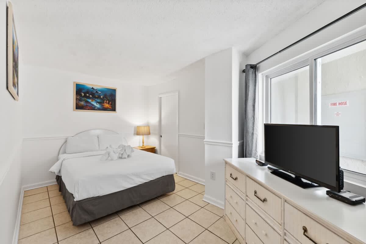 Moondrifter 608 – Bedroom with a queen bed, dresser, TV, and window with curtains.