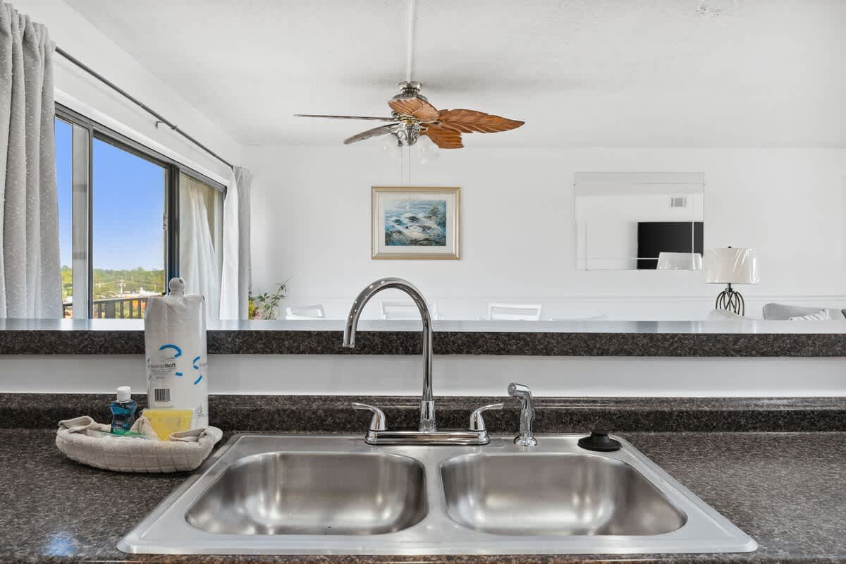 Moondrifter 608 – Modern kitchen sink with stainless steel basins, decorative ceiling fan, and view through large windows.
