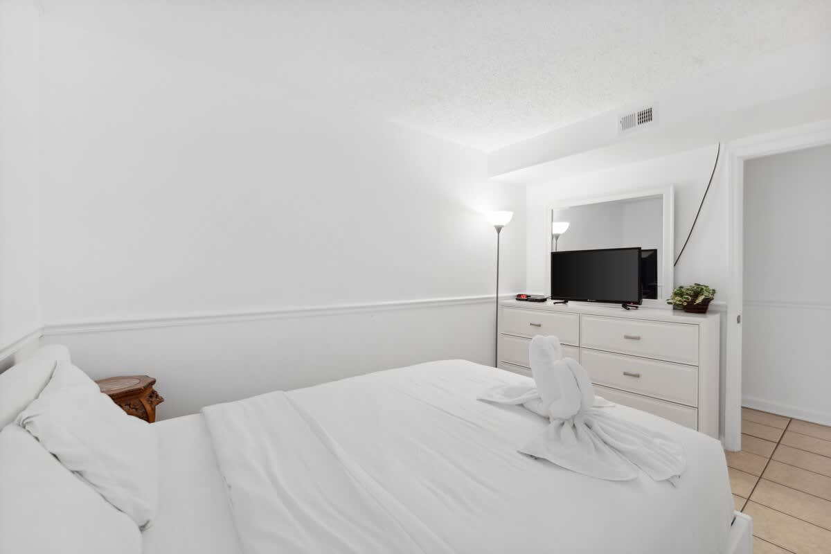 Moondrifter 608 – Bedroom with a double bed, dresser, TV, and lamp in a bright, simple decor.