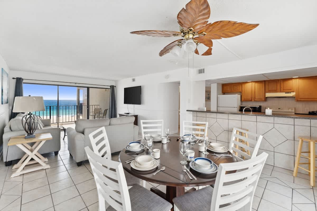 Moondrifter 608 – Living and dining area with ocean view, ceiling fan, gray sofas, and a round dining table set for six.