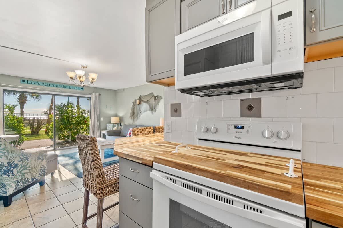 The Summit 105 – Cozy kitchen with white appliances, wooden countertop, and a view of greenery and beach through sliding glass doors.