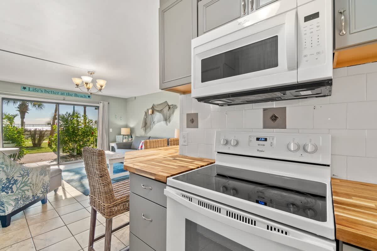 The Summit 105 – Kitchen area with white appliances, wooden countertops, and open view to a patio with greenery and beach.
