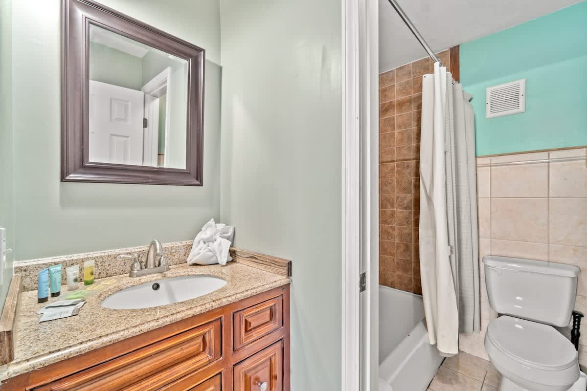 The Summit 105 – Bathroom with a sink, mirror, shower, and toilet, featuring light green walls and granite countertop.