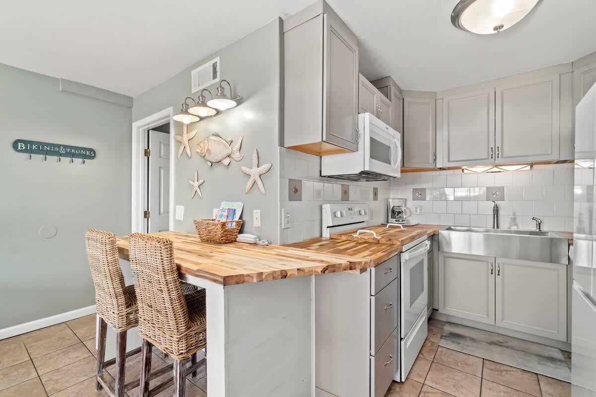 The Summit 105 – Kitchen with gray cabinets, stainless steel appliances, wooden countertop, and woven bar stools.