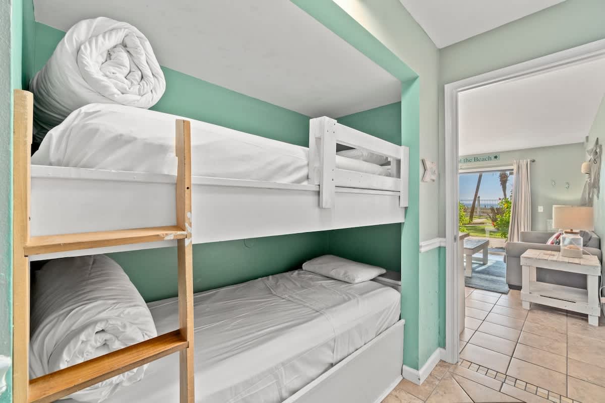 The Summit 105 – Bunk beds in a pastel-painted room with a view of palm trees through an open door.