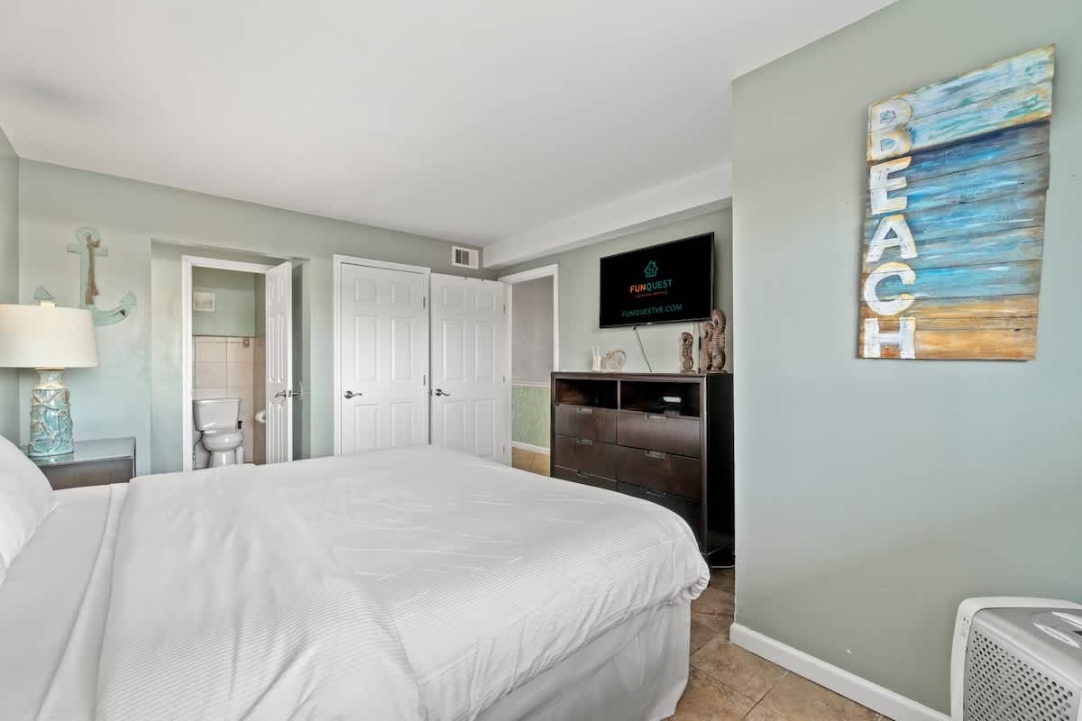 The Summit 105 – Bedroom with a queen bed, dresser, TV, and a bathroom doorway.
