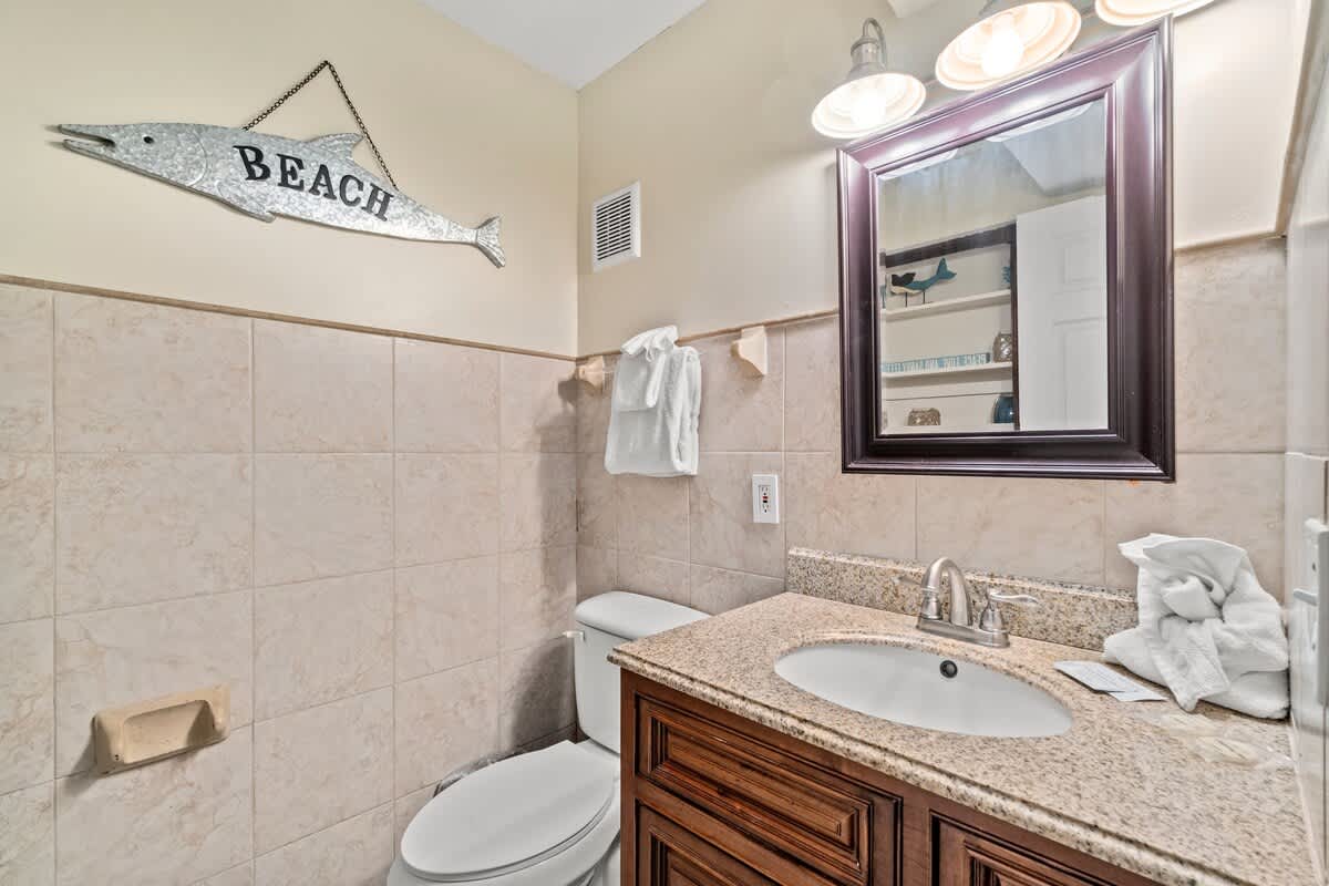 The Summit 105 – Bathroom with beige tiles, wooden cabinet, mirror, and beach-themed decor.