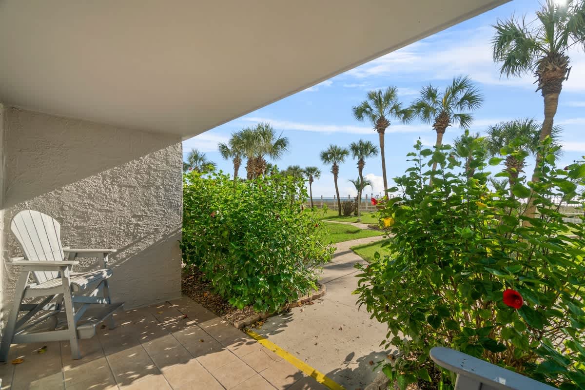 The Summit 105 – Covered patio with a grey chair, overlooking greenery and palms towards the beachfront.