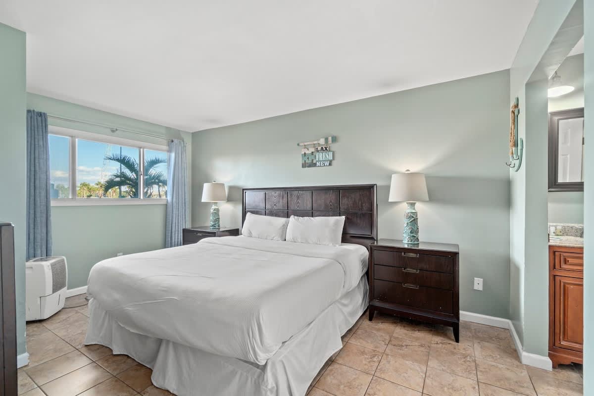 The Summit 105 – Cozy bedroom with a queen bed, lamps, and window view of palm trees.