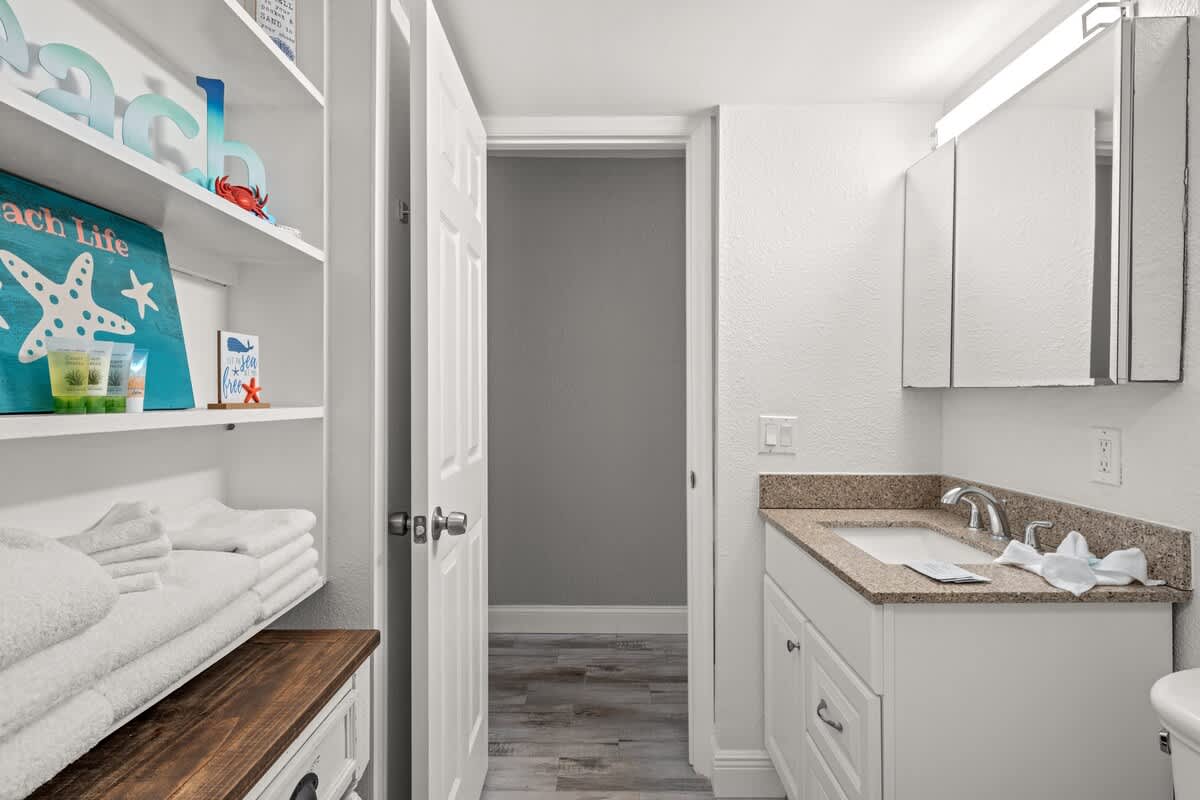 The Summit 228 – Bathroom with a sink, vanity, towels, shelving, and a door leading to another room.