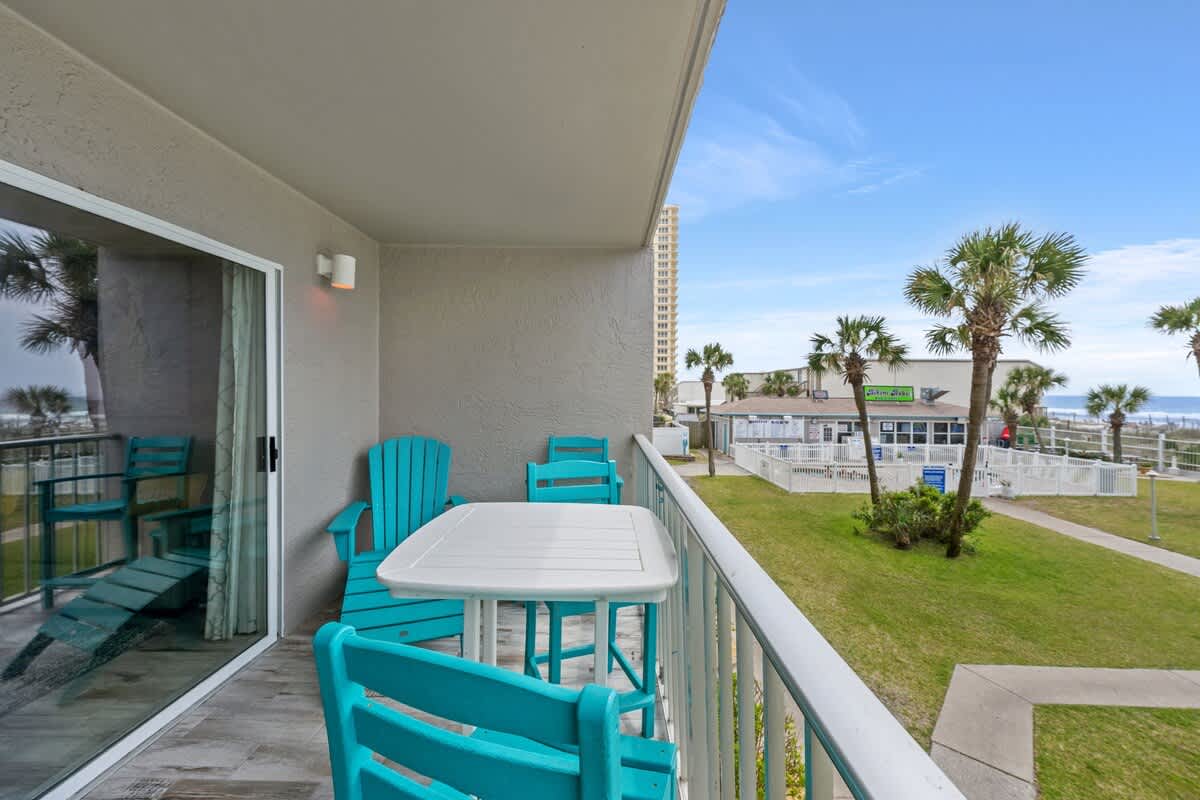 The Summit 228 – Balcony with turquoise chairs and table, overlooking green lawn and palm trees.