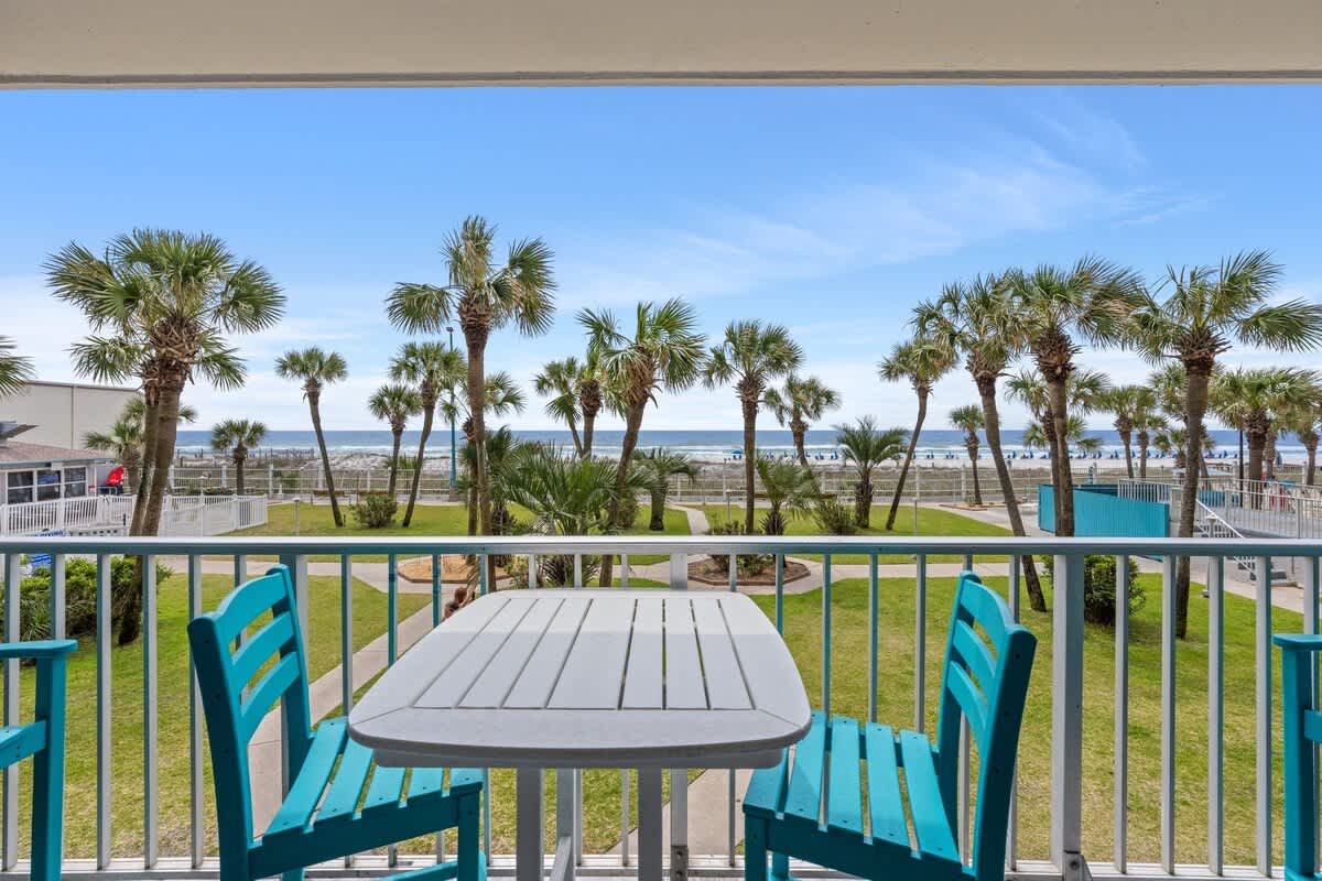 The Summit 228 – View from a balcony with turquoise chairs overlooking palm trees and the ocean.