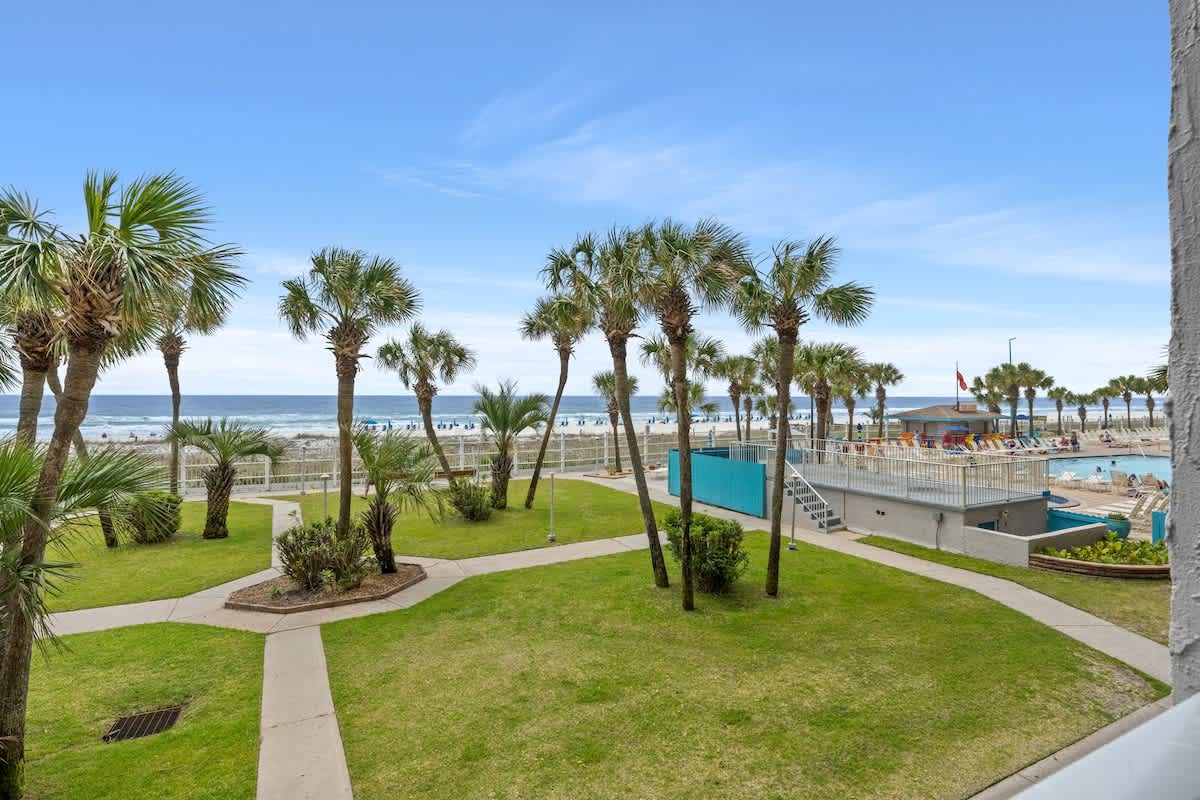 The Summit 228 – Ocean view from a balcony with palm trees and a pool area below.
