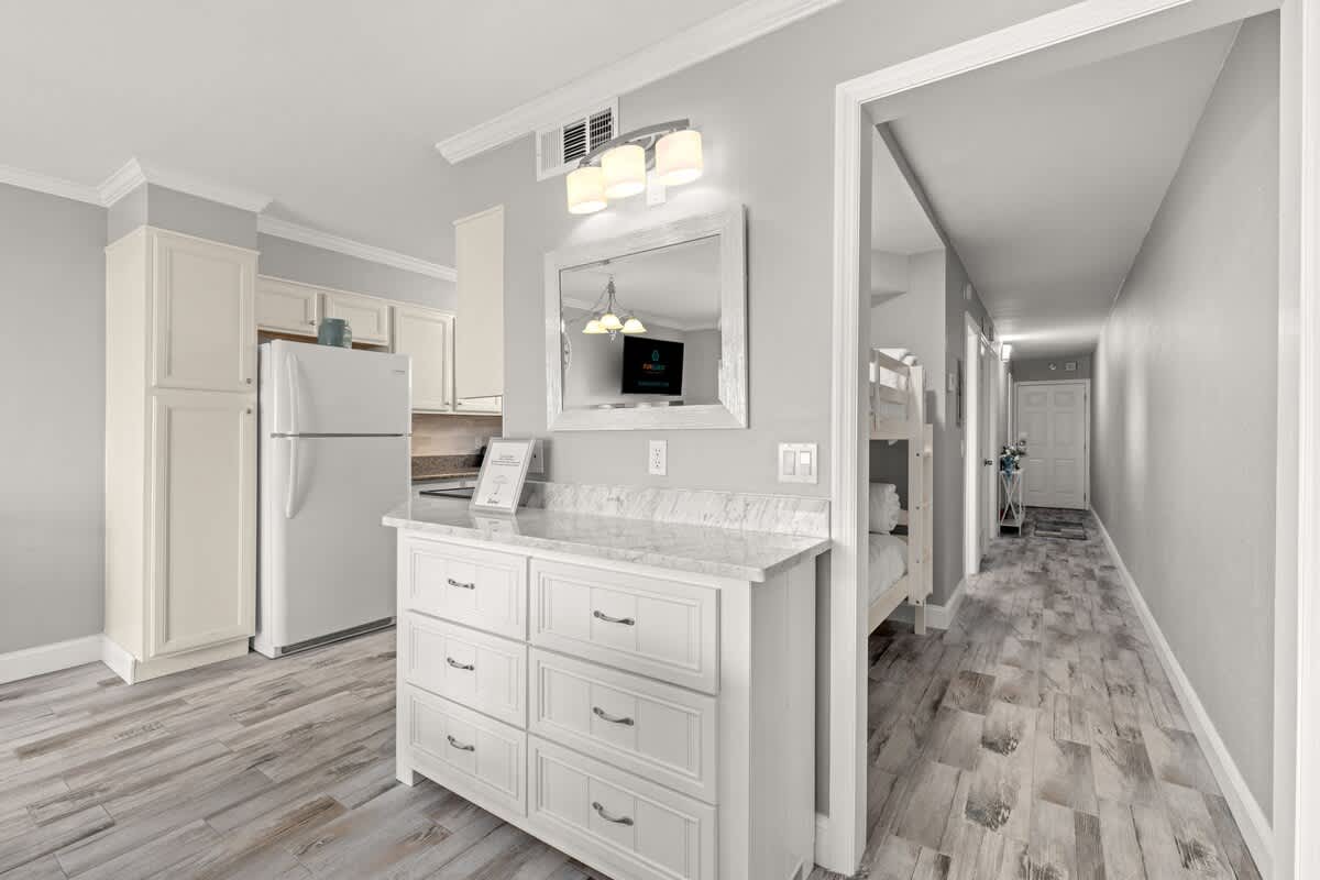 The Summit 228 – Interior view of a vacation rental kitchen with white cabinets, marble countertop, and a hallway leading to a bedroom.